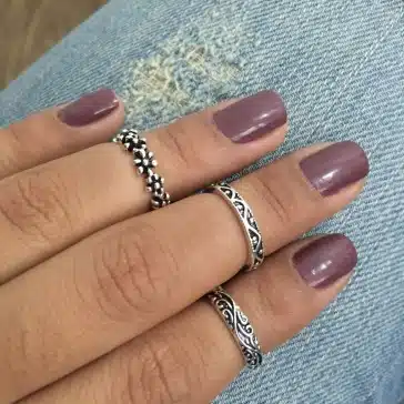 imagem ampliada de uma mão com as unhas pintadas de roxo com anéis de prata