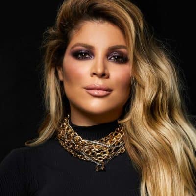 Mulher loira, com roupa preta e vários colares.