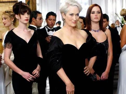 imagem do filme o diabo veste prada com anne hathaway e maryl streep usando um vestido preto dentro de um salão