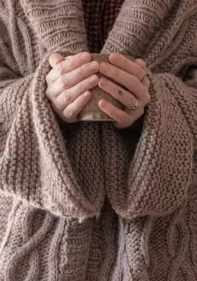mulher com blusa de tricô e copo de café nas mãos