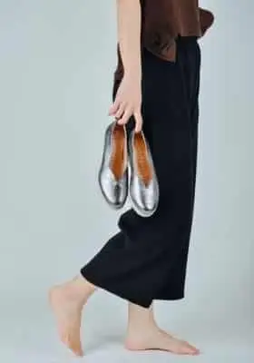 mãos segurando sapatos prateados ao lado de pés descalços